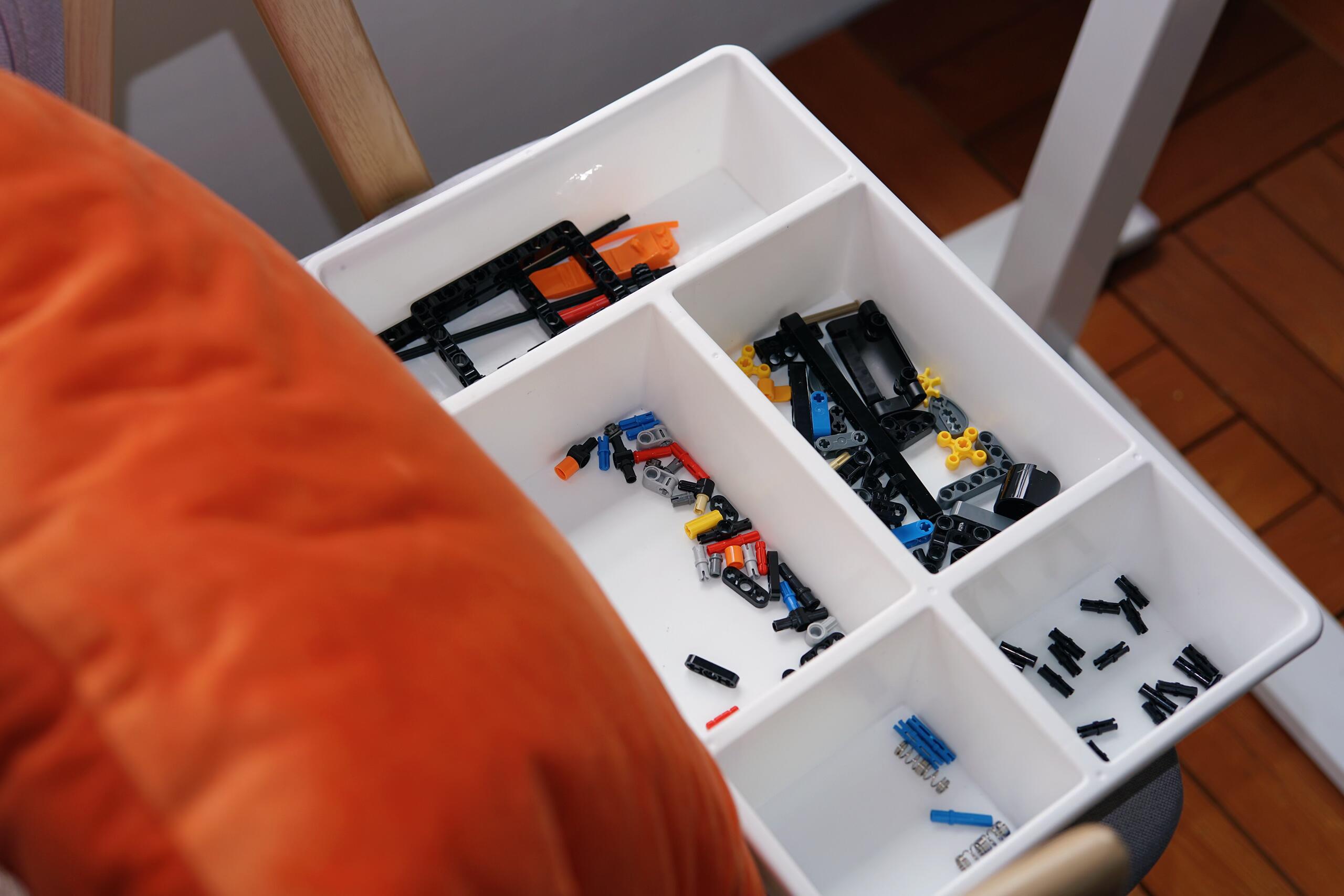 Sorted MOC parts in white compartment trays — pins, axles, connectors and panels separated